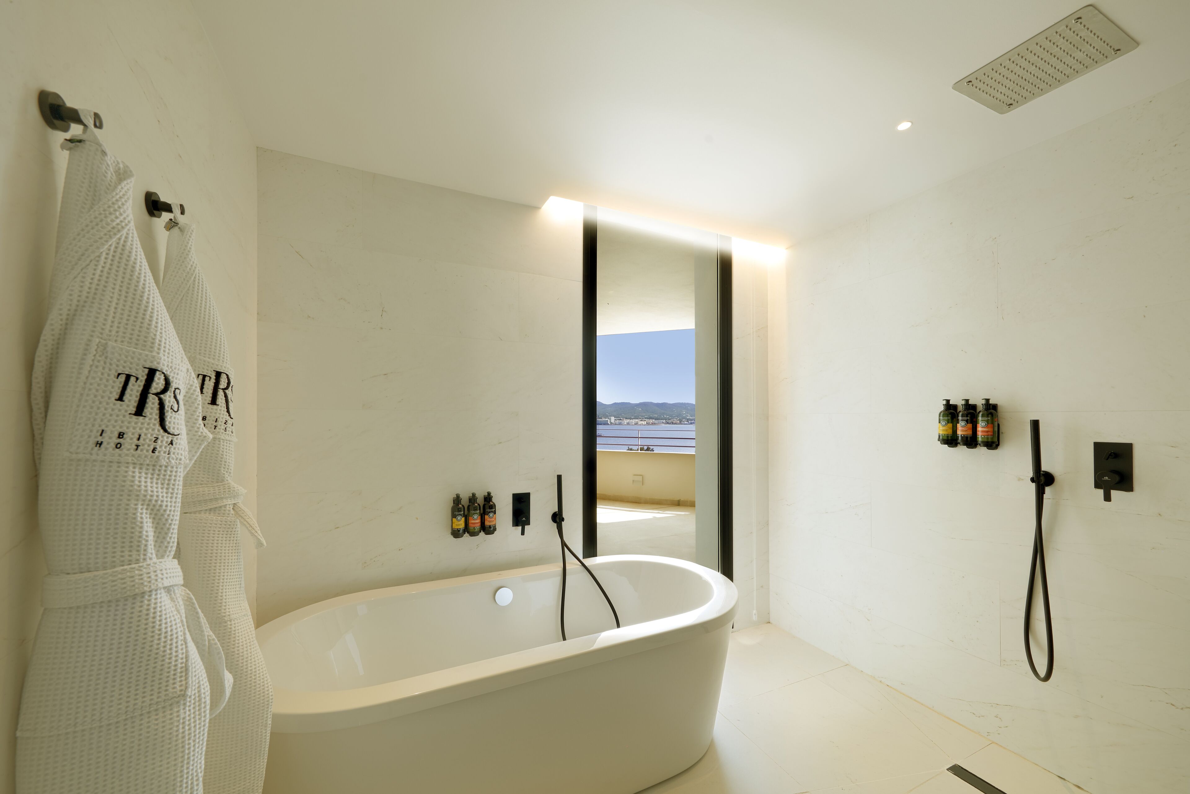 A modern bathroom with a freestanding bathtub, a large mirror, and a view of the sea.