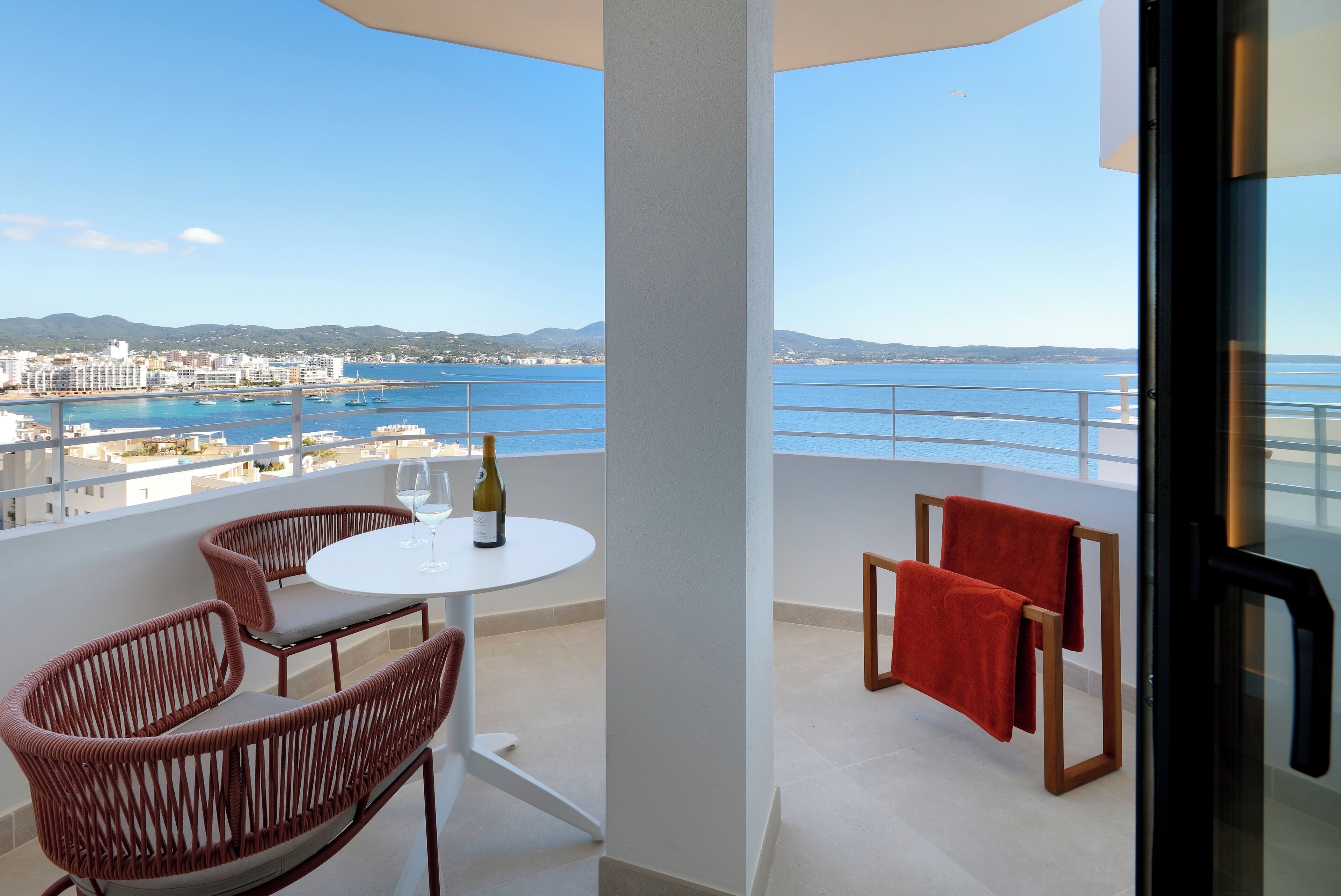 A balcony with wicker chairs, a small round table, and a bottle of wine.