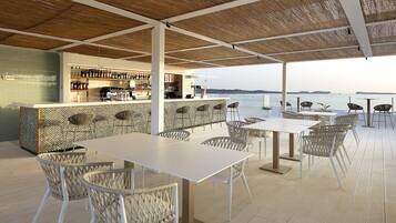 Zona de bar al aire libre con vistas al mar, que incluye una barra, asientos y suelo de baldosas.