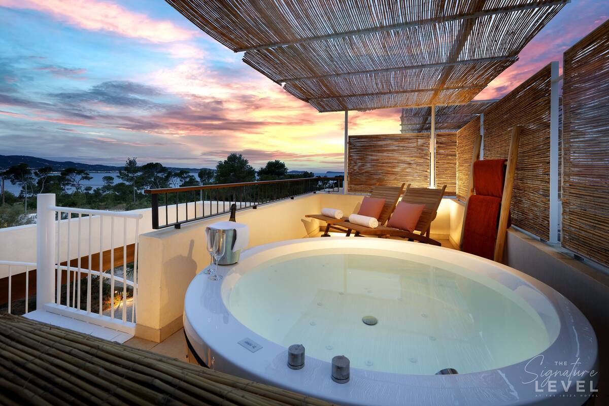 A hot tub with a view of the sunset, a wooden deck, and a lounge area with cushions.