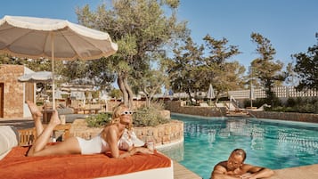 A poolside area with lounge chairs and umbrellas, a stone wall, and a clear blue pool.