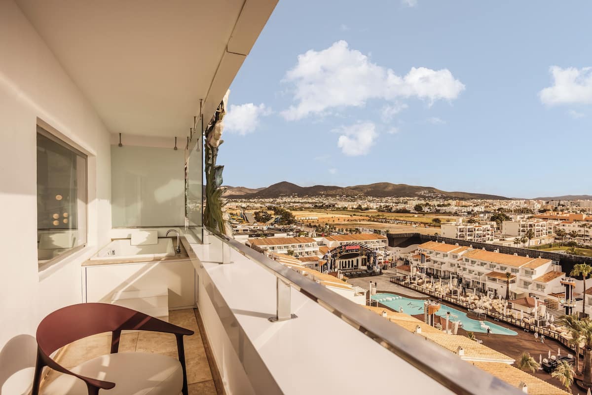 Ein Balkon mit Blick auf eine Küstenstadt, einen Pool und einen Stuhl.