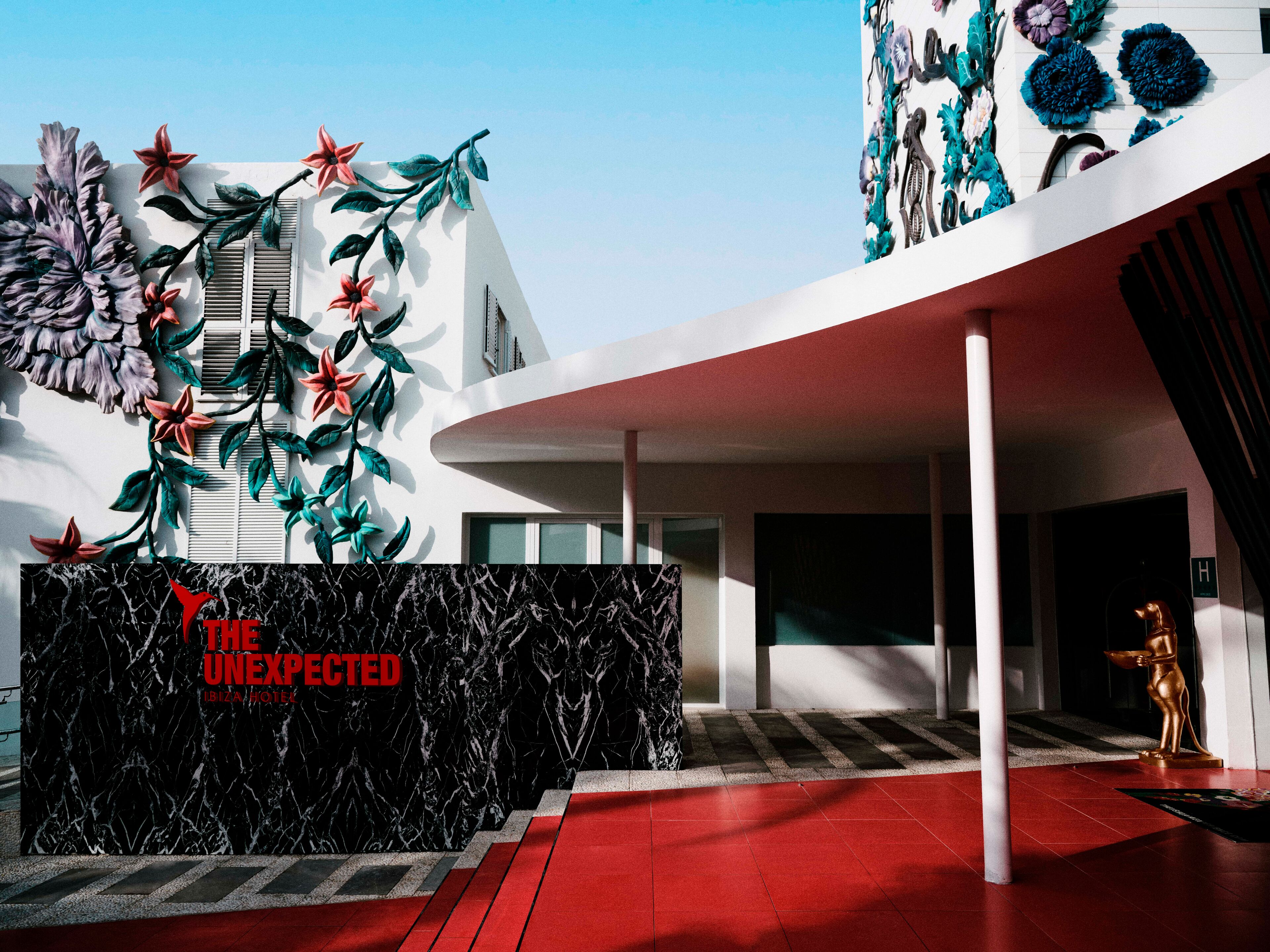 Un edificio moderno con una entrada destacada, una pared con textura de mármol y una alfombra roja que conduce a la puerta.