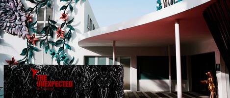 Un edificio moderno con una entrada destacada, una pared con textura de mármol y una alfombra roja que conduce a la puerta.