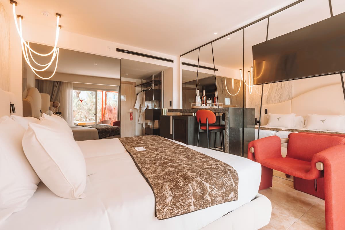 Ein modernes Hotelzimmer mit einem großen Bett, einem Schreibtisch, einem roten Sessel und einem großen Spiegel.