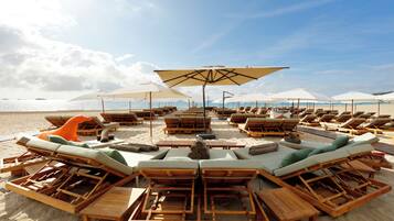 Eine Strandlounge mit Holzliegen, weißen Sonnenschirmen und freiem Blick auf das Meer.