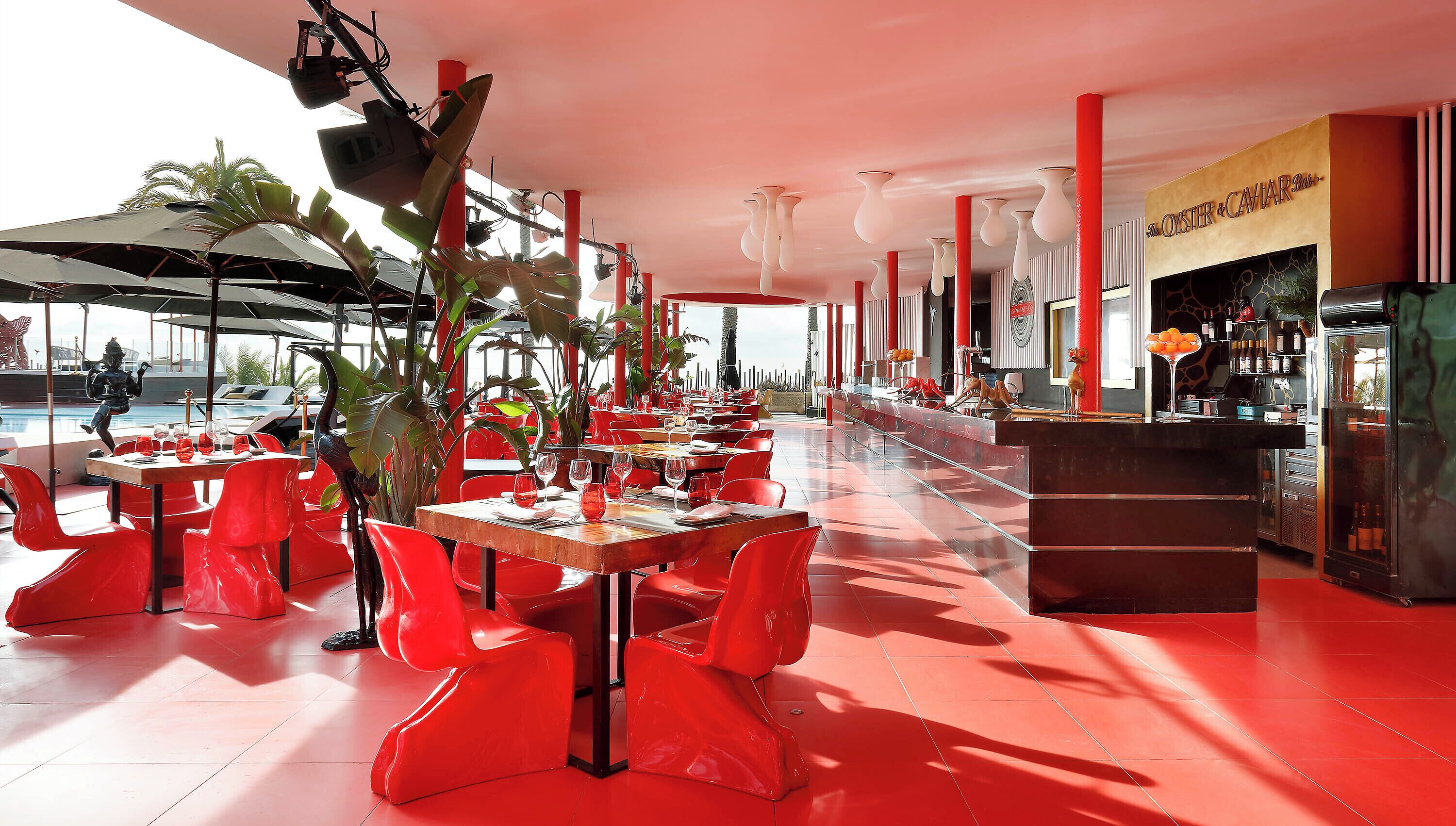 Ein Restaurant mit roten Stühlen und Tischen, einer Bar und einem Pool im Hintergrund.