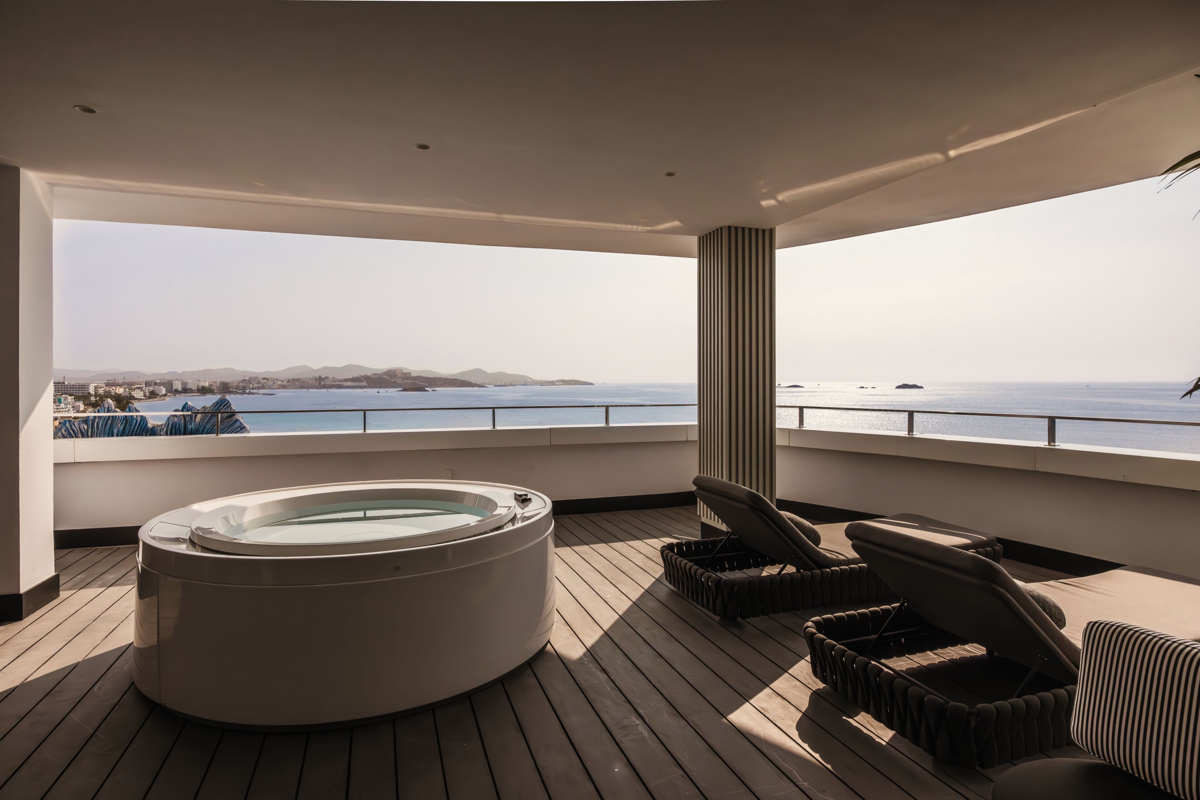 A deck with a hot tub, lounge chairs, and a view of the sea.