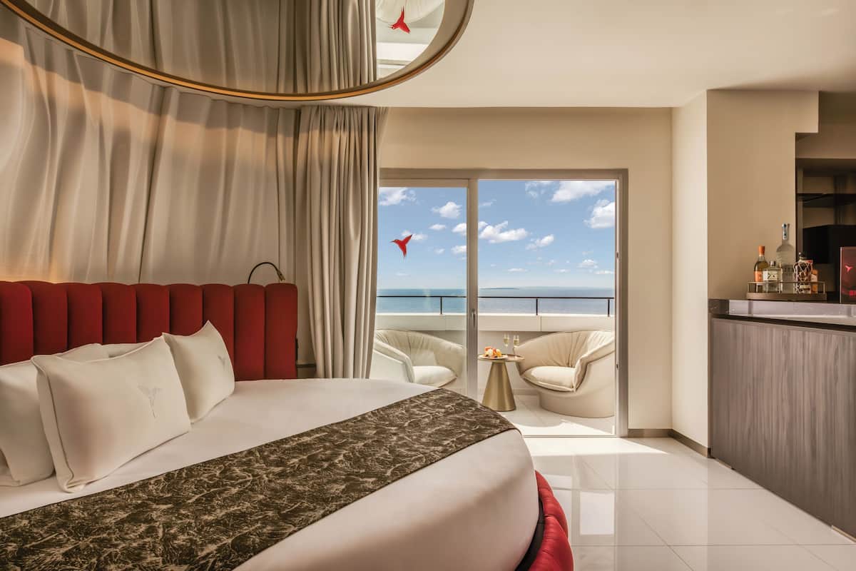 Ein Hotelzimmer mit Bett, einem Balkon mit Meerblick und einer kleinen Sitzecke.