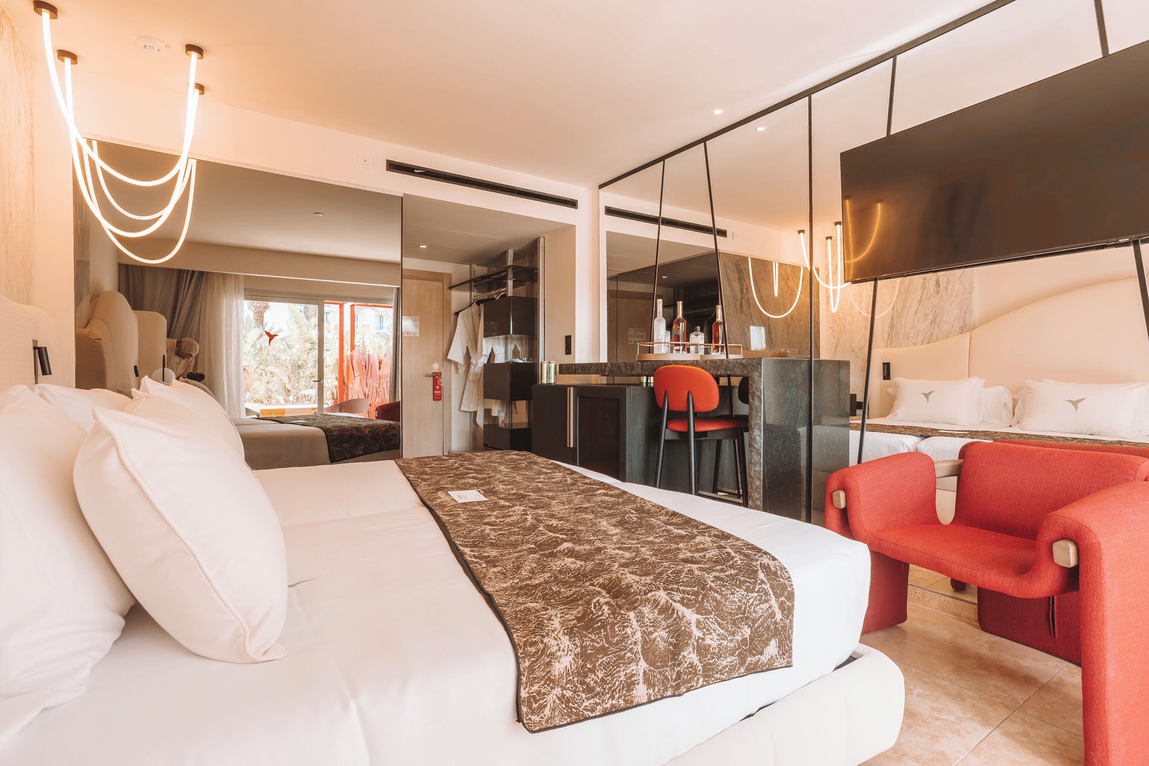 Ein modernes Hotelzimmer mit einem großen Bett, einem Schreibtisch, einem roten Sessel und einem großen Spiegel.