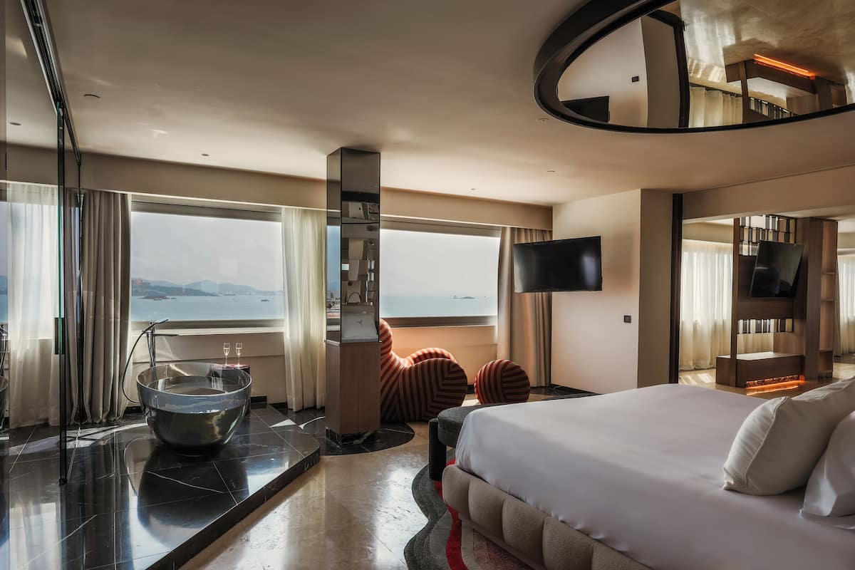 Ein modernes Hotelzimmer mit einem großen Bett, einer Sitzecke mit Blick, einem großen Fenster und einem Flachbildfernseher.