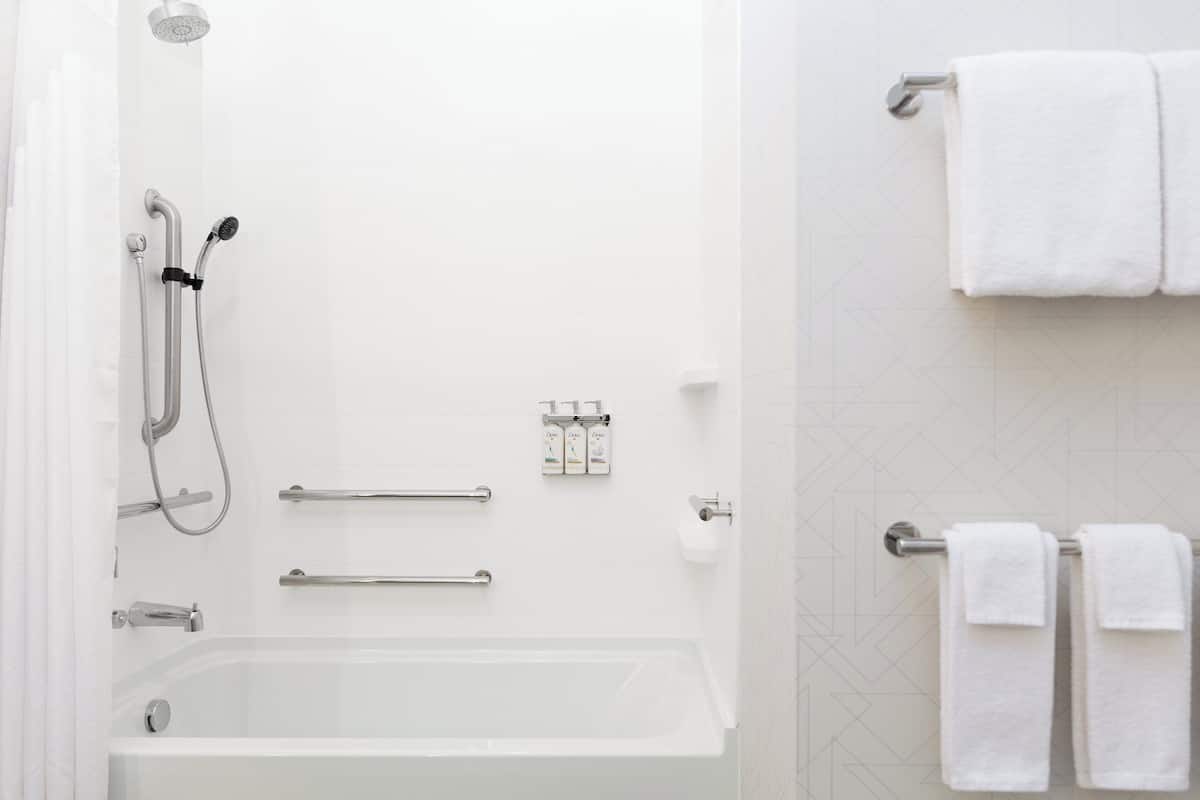 Un baño moderno con bañera, ducha, barras de apoyo y toallas blancas.