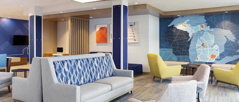 Un moderno vestíbulo de hotel con un sofá, sillas, un mural de un mapa y un televisor en la pared.