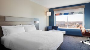 Una habitación de hotel con una cama grande, un escritorio, una silla y una ventana con vista a la ciudad.