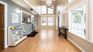 A spacious hallway with wooden flooring, a chandelier, and large windows offering views of the outside. - Gator Town Inn (Gainesville)
