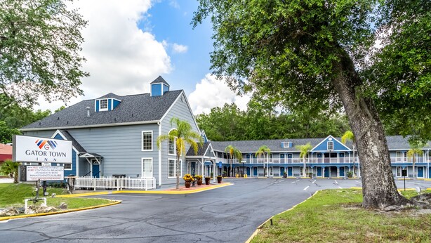 A motel with a Gator Town Inn sign, a fenced parking area, and a row of blue buildings with balconies.