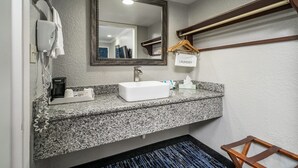 A bathroom with a granite countertop, a white sink, a mirror, a towel rack, a wooden hanger, and a towel hanging on the rack. - Gator Town Inn (Gainesville)
