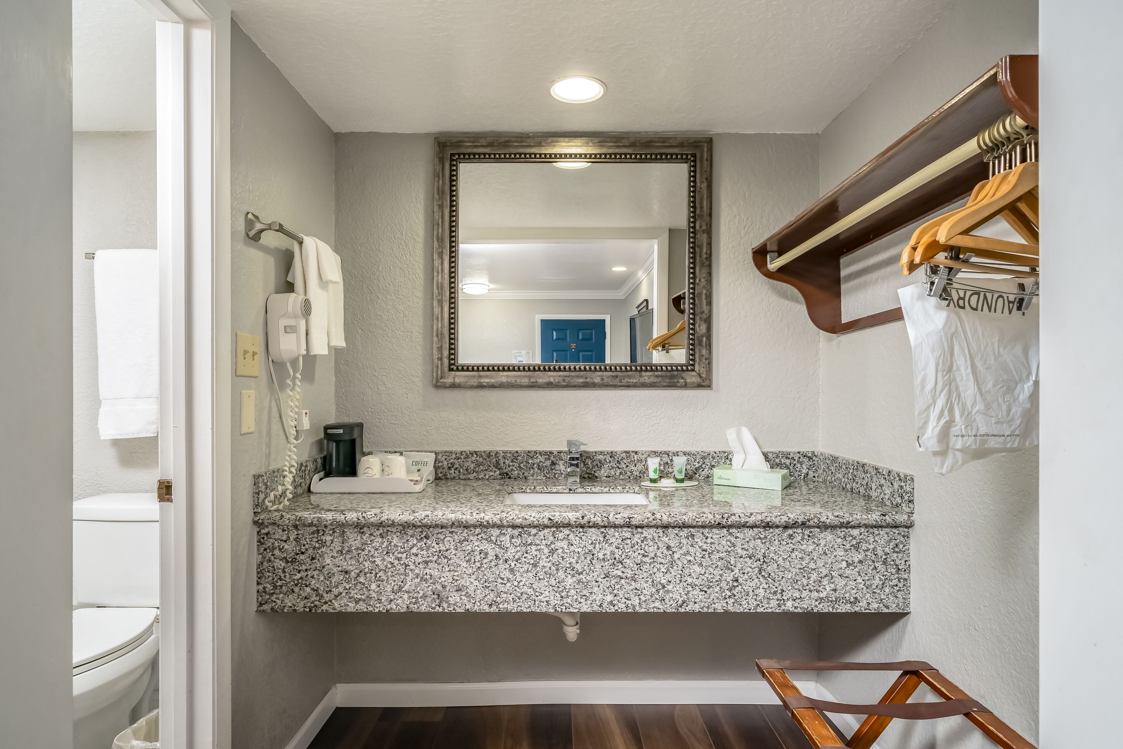 A bathroom with a granite countertop, a white sink, a mirror, and a towel rack.
