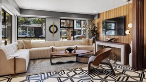 A modern living room with a sectional sofa, a coffee table, a TV mounted on the wall, and a large window providing a view of the outside. - Infinity Hotel San Francisco, Tapestry Collection by Hilton (San Francisco)