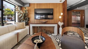 A modern hotel lobby with a sofa, a wooden reception desk, a flat-screen TV, and an elevator. - Infinity Hotel San Francisco, Tapestry Collection by Hilton (San Francisco)