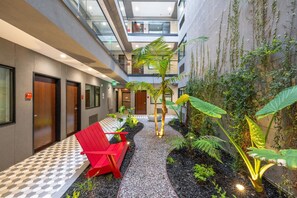 Un pasillo de hotel con una silla roja, una palmera y una pared cubierta de plantas trepadoras.