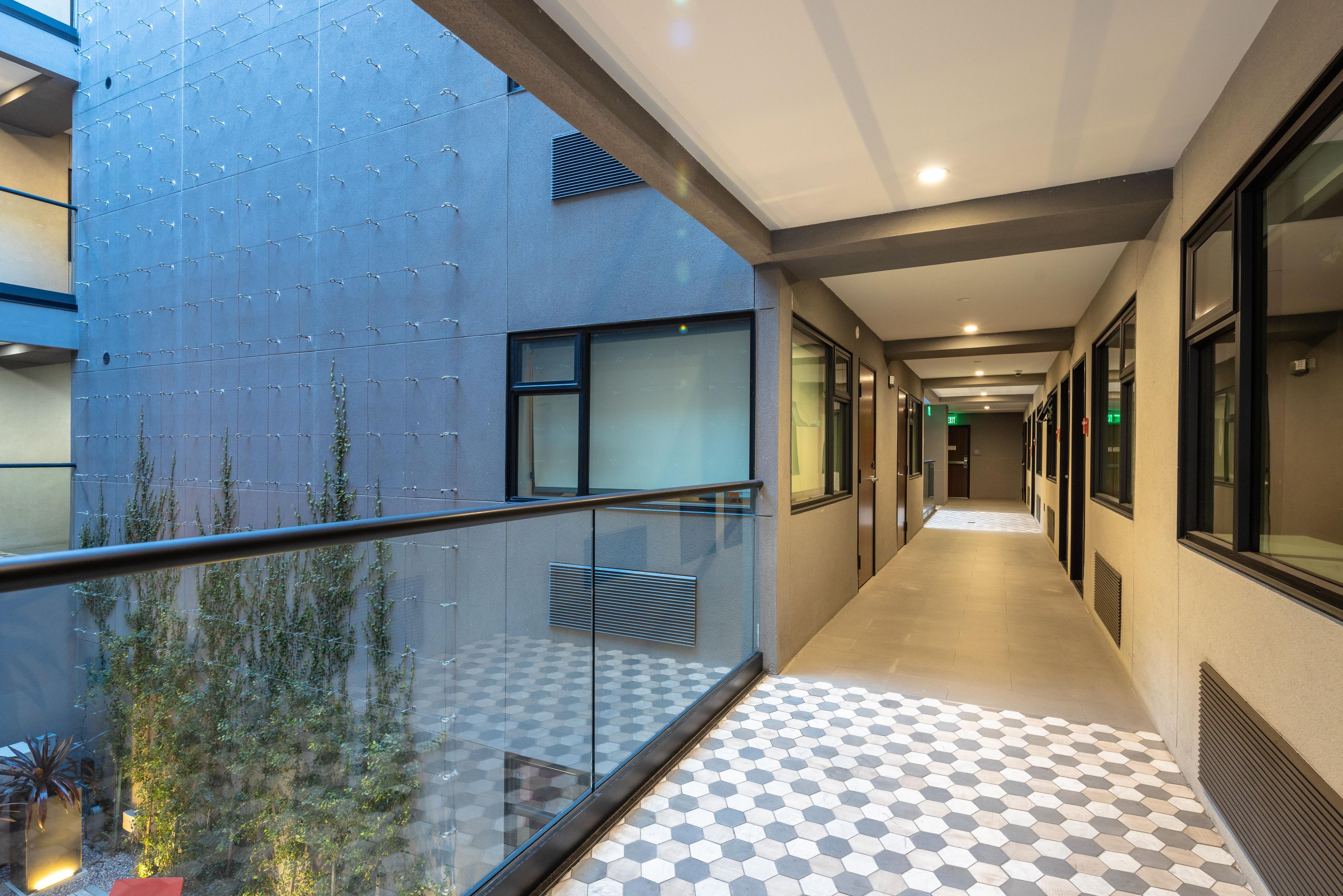 A corridor with a glass balustrade, a patterned floor, and a building facade with a grid of hooks.