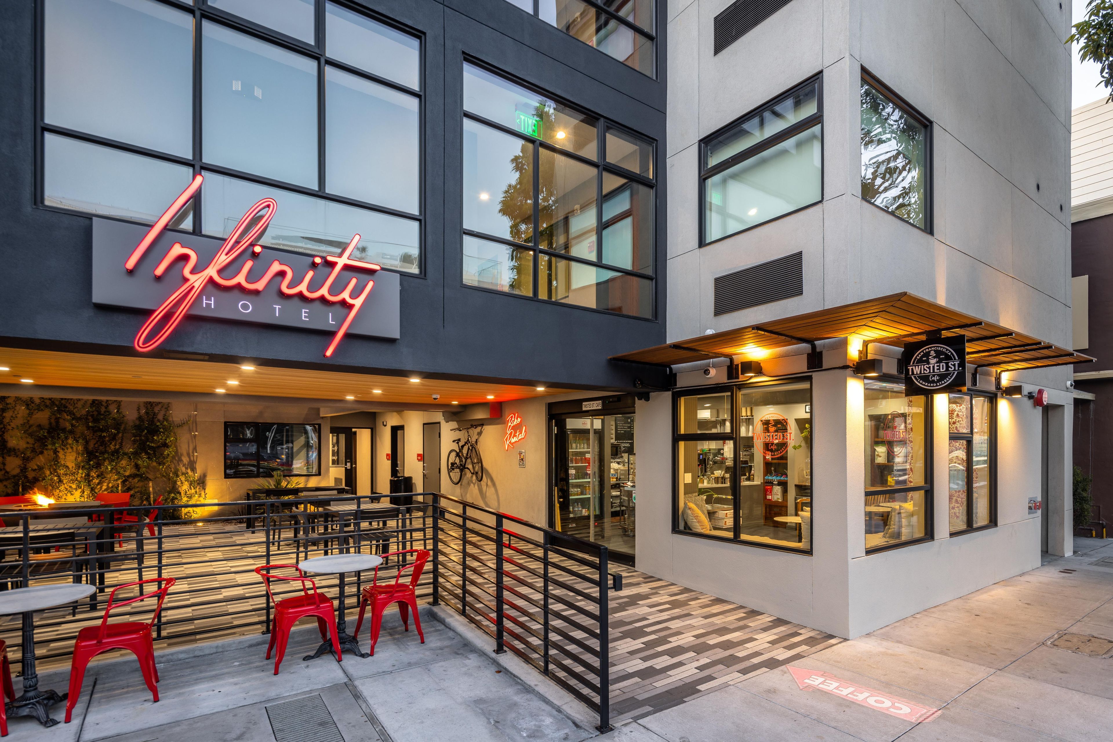 A hotel exterior with outdoor seating, a bike rental sign, and a storefront with a cafe.