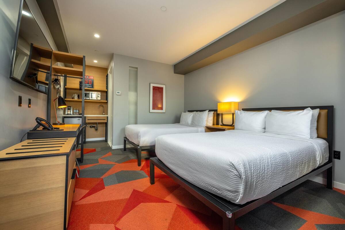 A hotel room with two beds, a desk, a chair, a TV, and a bathroom.