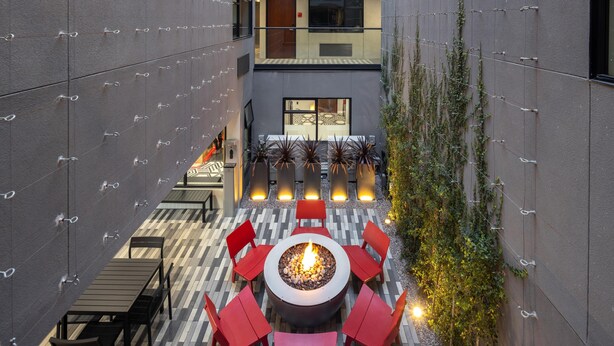 An outdoor patio with a fire pit, red chairs, and a tiled floor. - Infinity Hotel San Francisco, Tapestry Collection by Hilton (San Francisco)