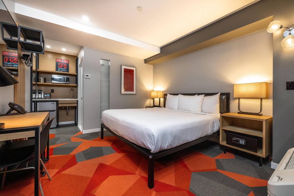 A hotel room with a bed, desk, microwave, and a small kitchenette.
