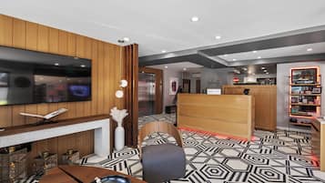 A hotel lobby with a modern design, featuring a flat-screen TV, a fireplace, a reception desk, and a patterned floor.