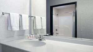 Un baño moderno con un lavamanos blanco, un espejo grande y una ducha con mampara de vidrio.