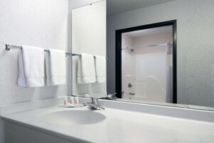 Un baño moderno con un lavamanos blanco, un espejo grande y una ducha con mampara de vidrio.