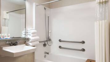 A bathroom with a sink, mirror, shower, and grab bars.
