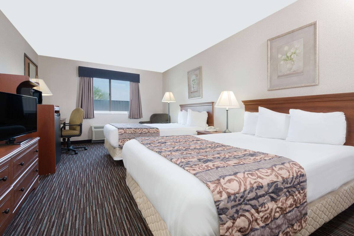 A hotel room with a bed, two bedside tables, a TV, a chair, a desk, and a window with curtains.
