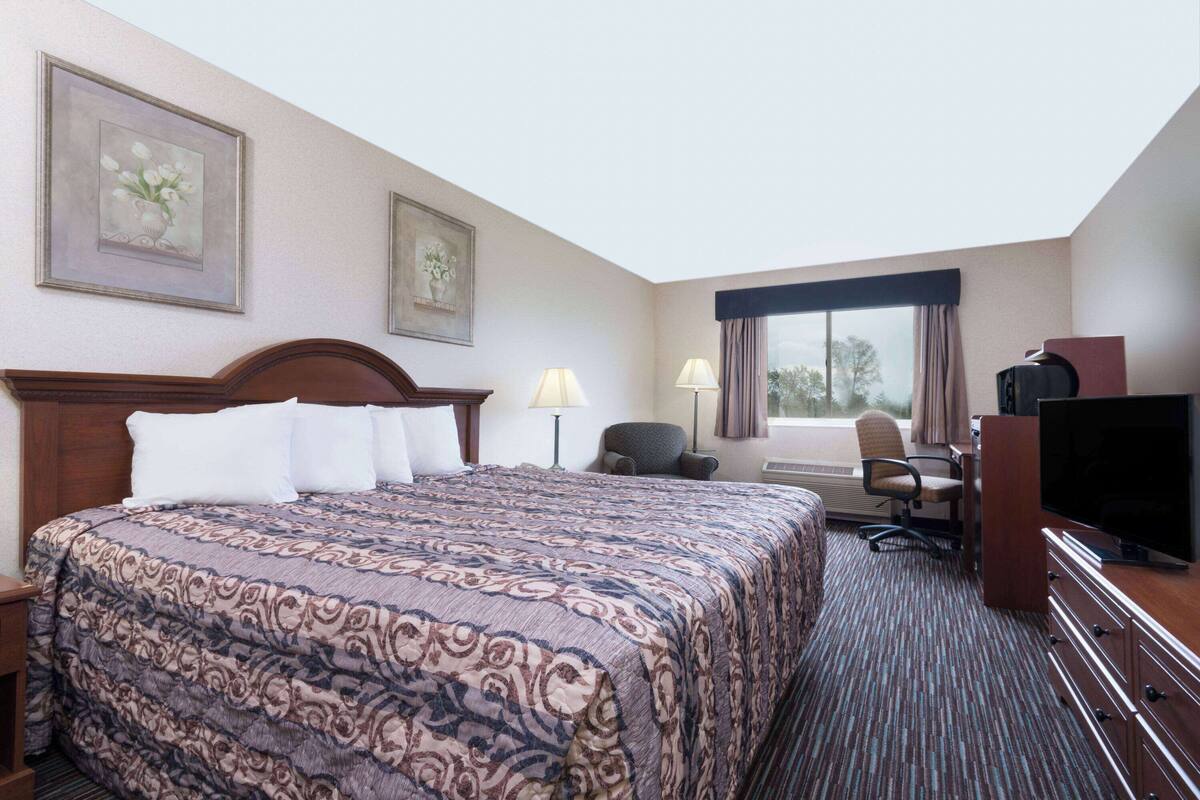 A hotel room with a large bed, a desk with a chair, a television, and two lamps.