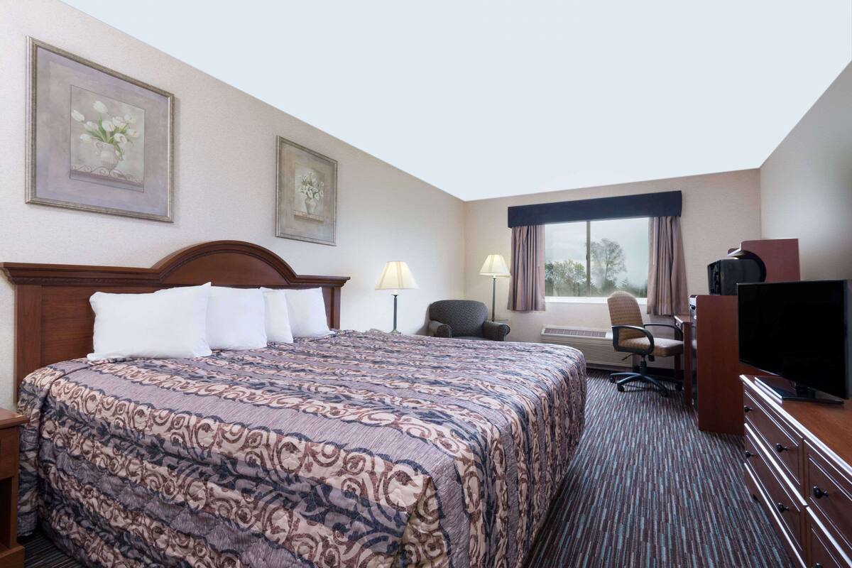 A hotel room with a large bed, a desk with a chair, a television, and two framed pictures on the wall.