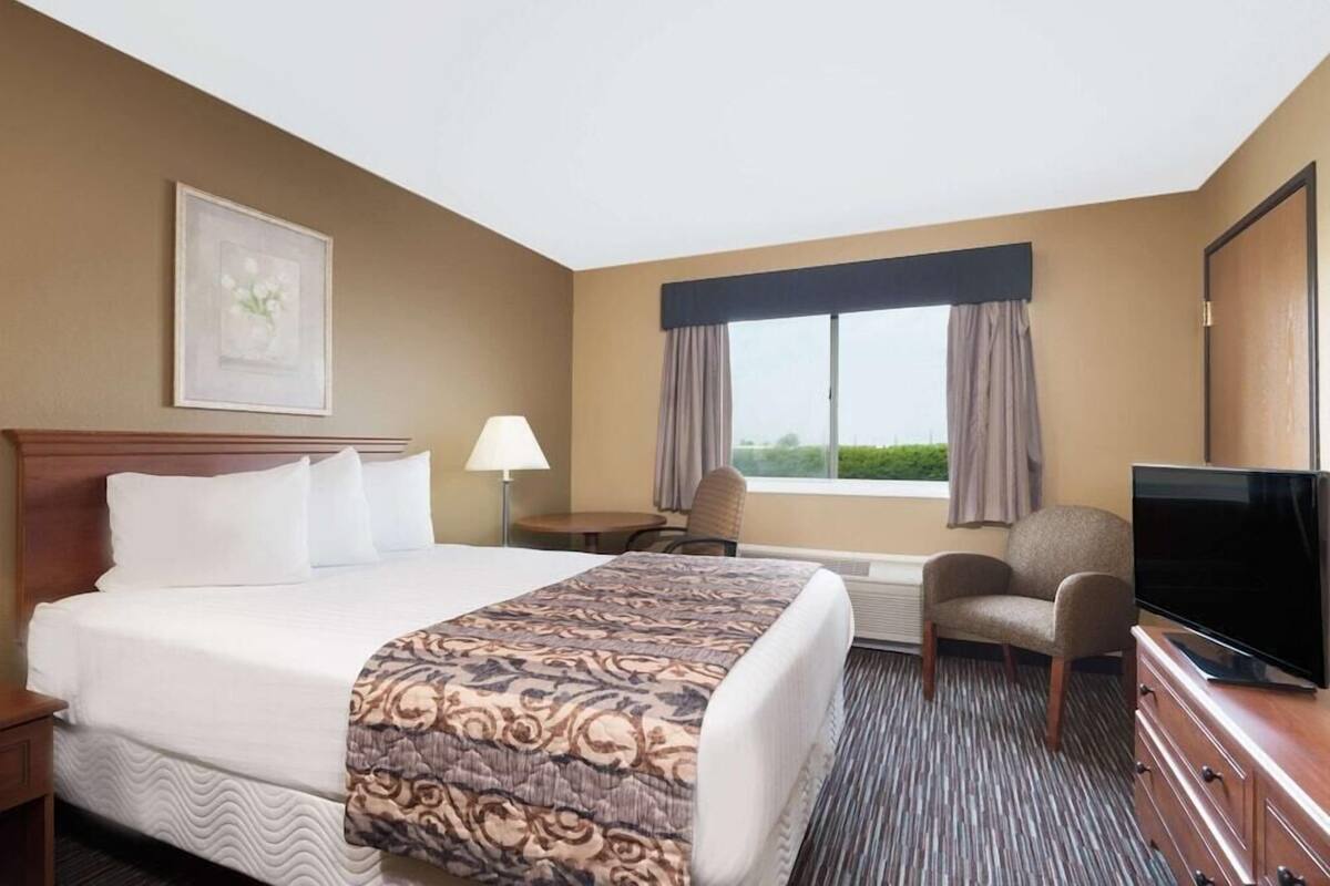 A hotel room with a bed, a desk, a chair, a television, and a window with curtains.