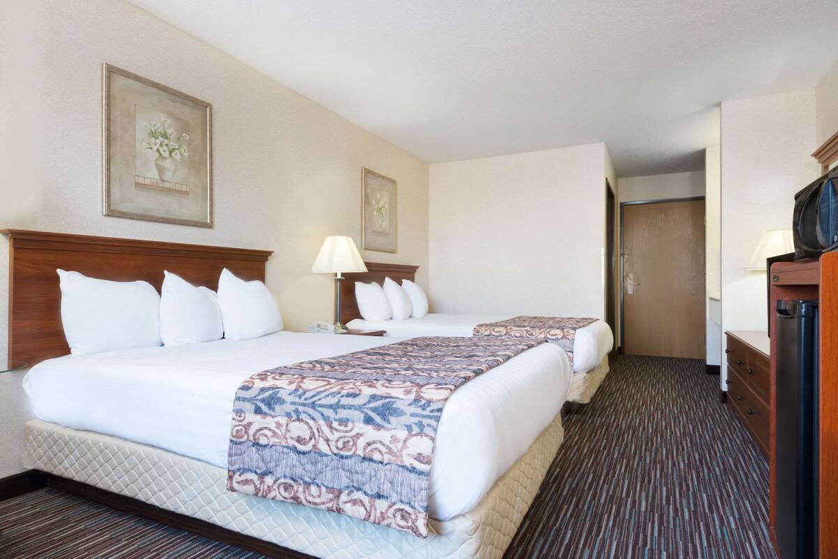 A hotel room with two beds, a wooden headboard, a bedside table with a lamp, and a television.