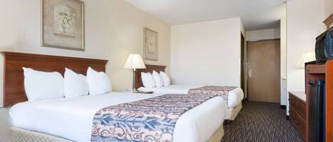 A hotel room with two beds, a wooden headboard, a bedside table with a lamp, and a television.