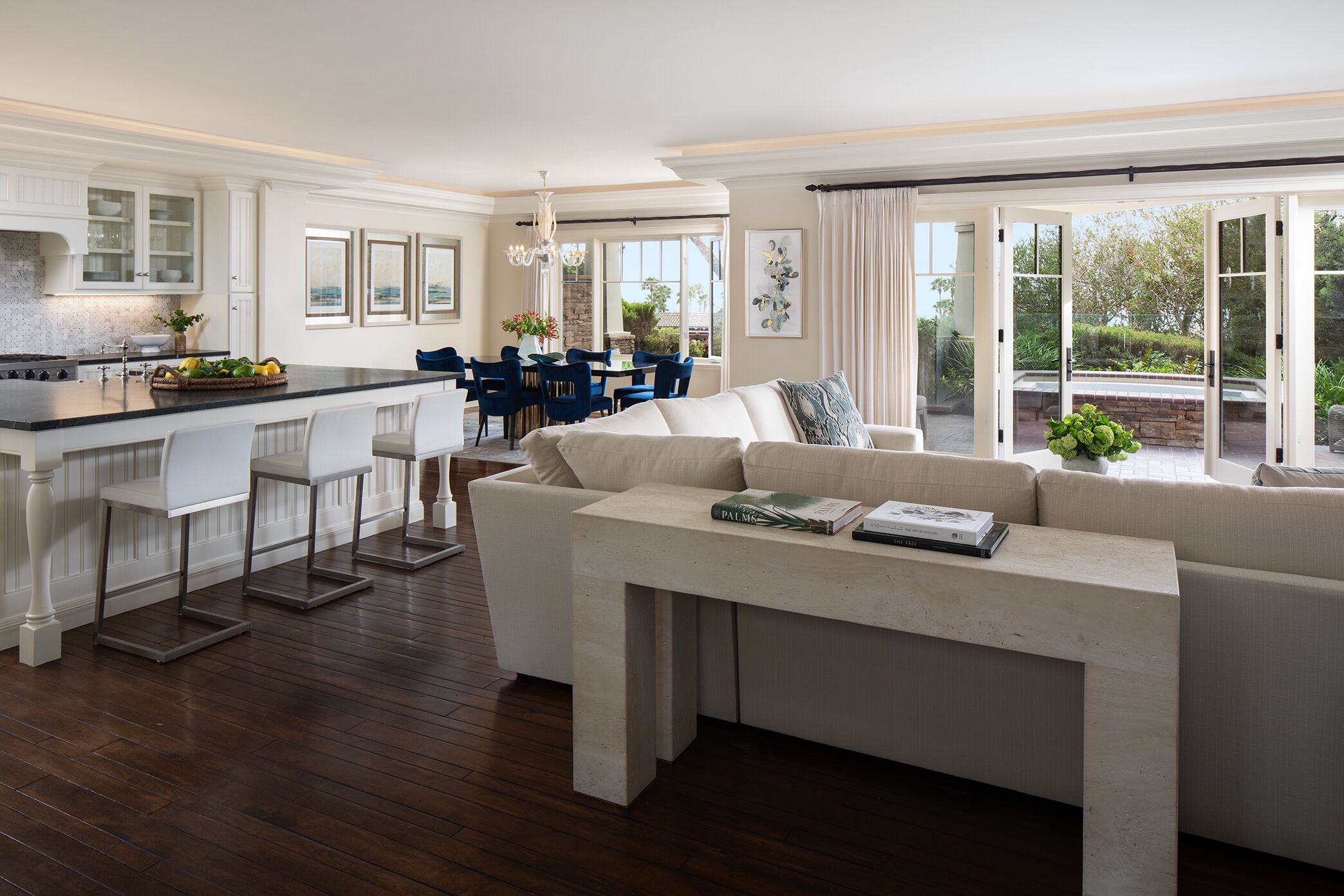A modern kitchen with a central island, dining area with blue chairs, and a large window with a view of greenery.