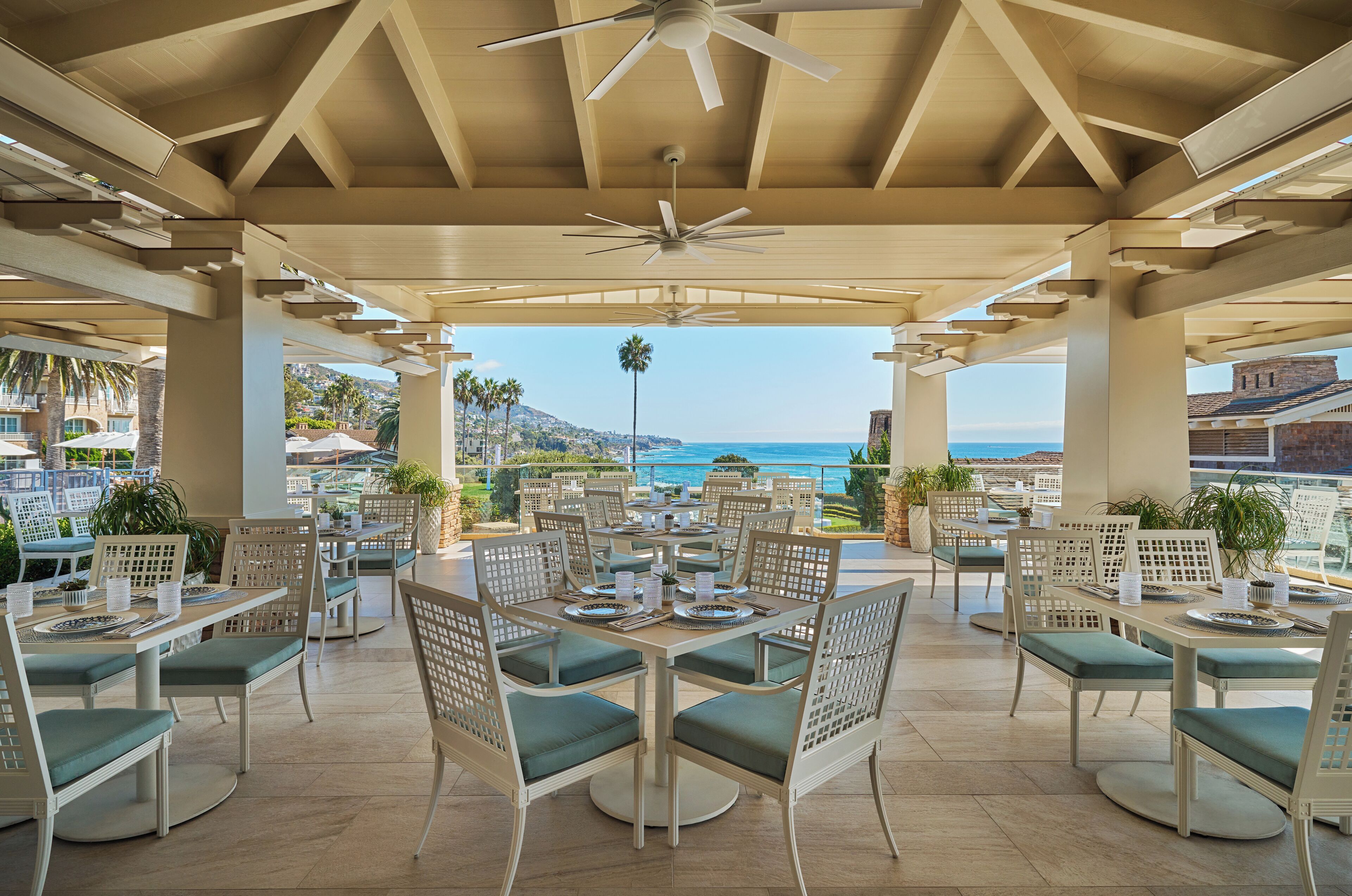 An outdoor dining area with tables and chairs, a ceiling fan, and a view of the ocean.