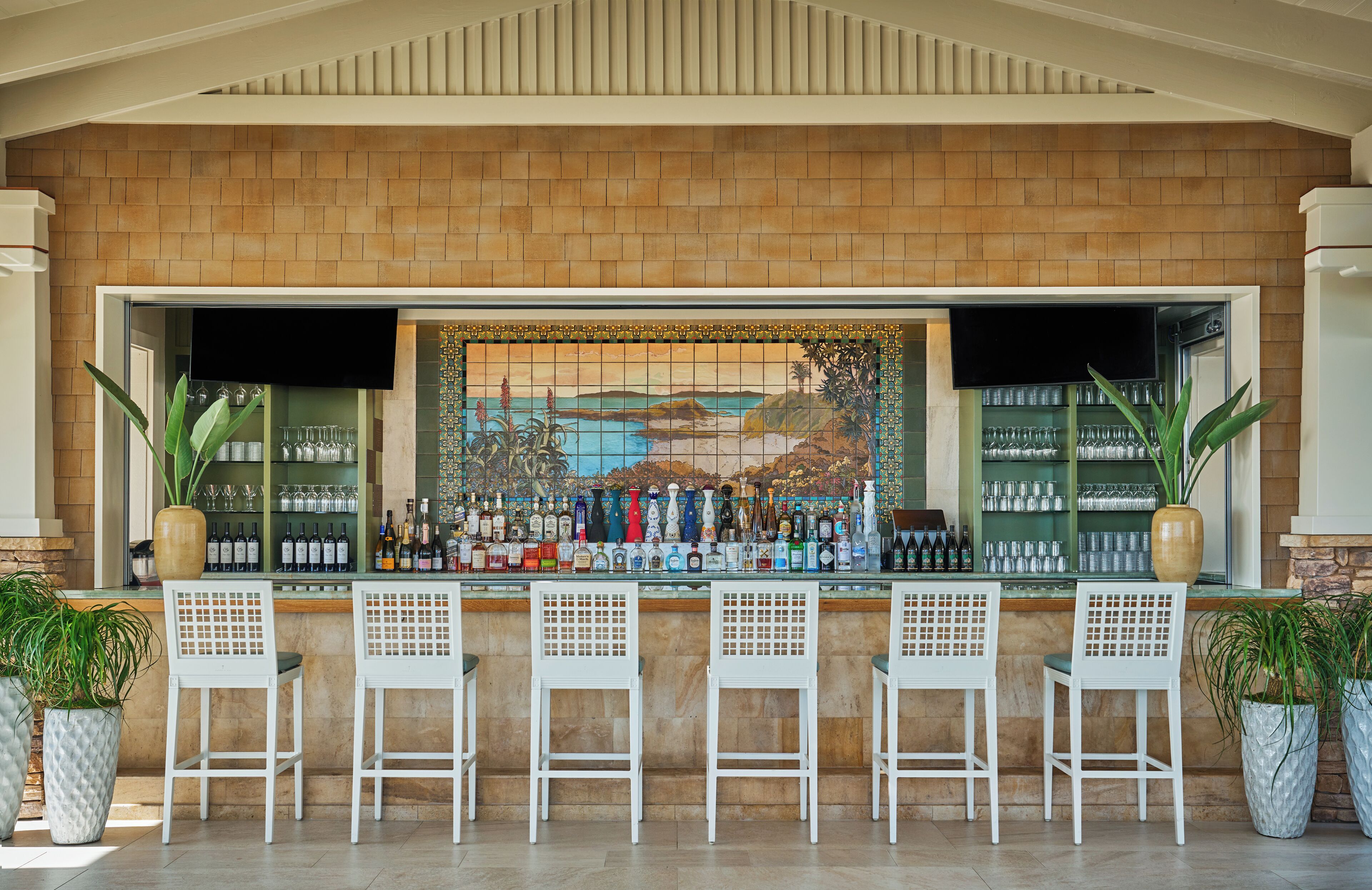 A bar area with a tiled backsplash, bar stools, and a variety of bottles and glasses.