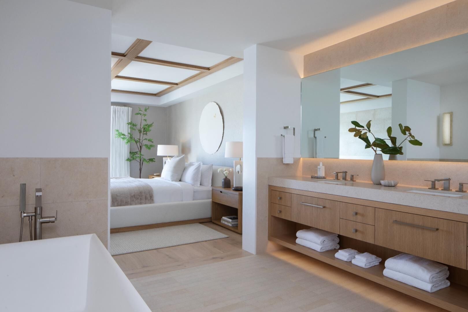 Una habitació d'hotel moderna amb un llit gran, un bany separat amb banyera, un mirall gran i una planta en test.