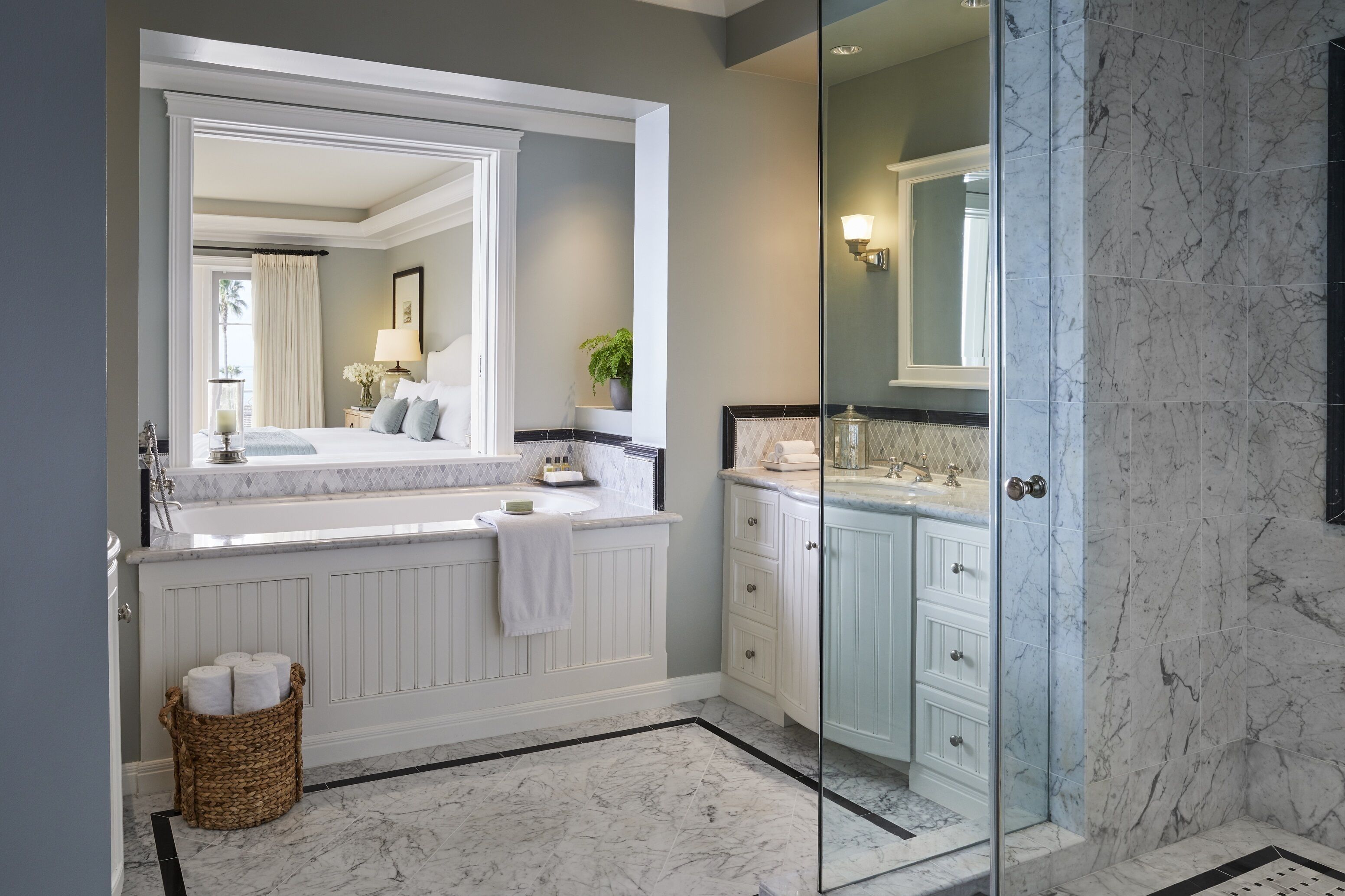 A modern bathroom with a large mirror, white vanity, marble flooring, and a glass shower enclosure.