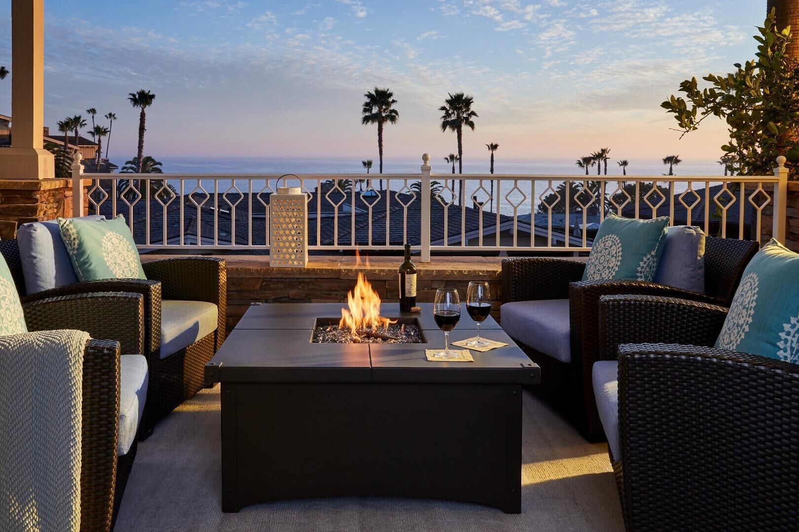 An outdoor seating area with wicker furniture, a fire pit, and a view of the ocean.