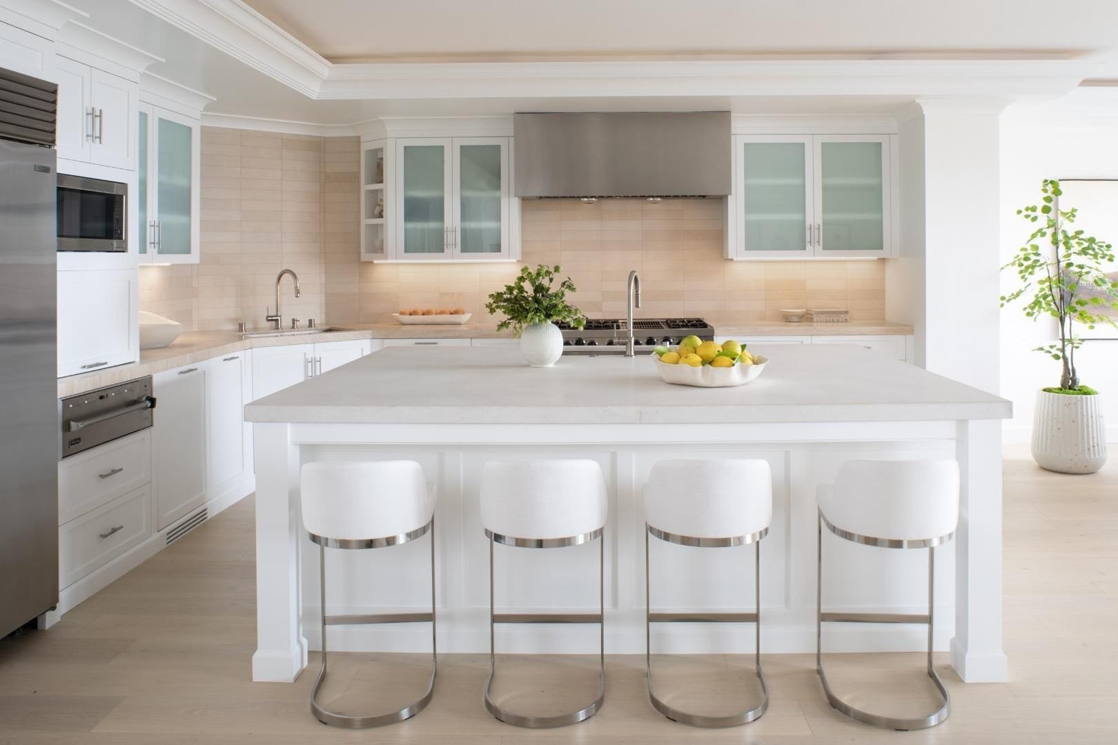 A modern kitchen with white cabinetry, a central island with bar stools, a stainless steel range, and a large window.