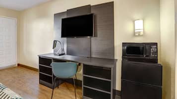 Una habitación compacta con una televisión de pantalla plana montada en la pared, un escritorio con una silla, un microondas y un refrigerador.