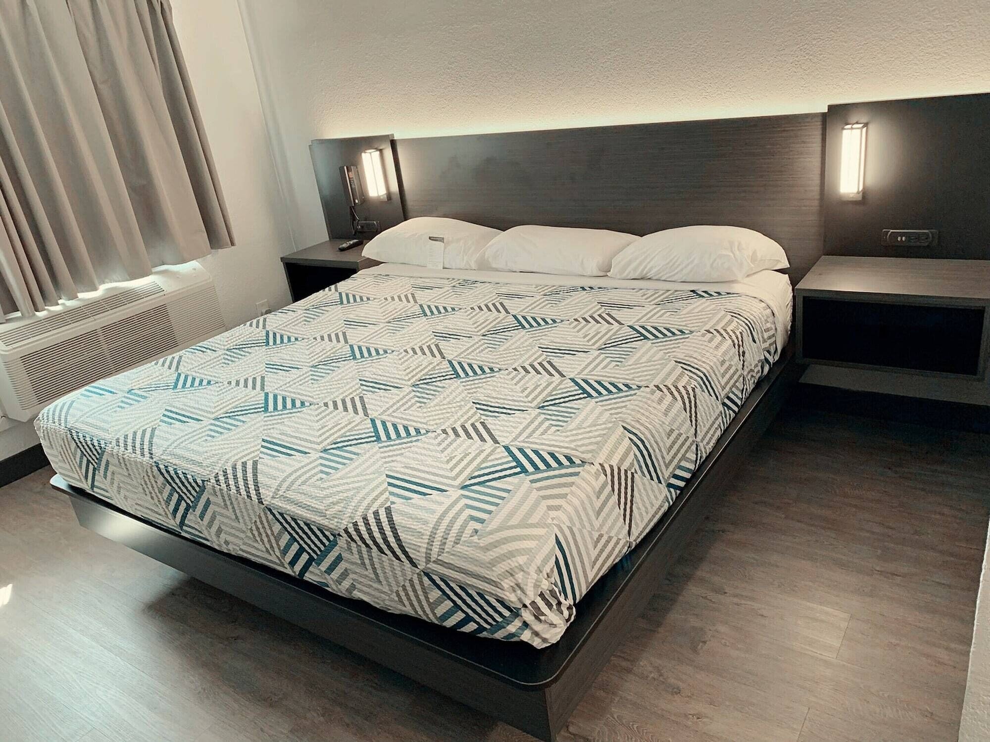 Une chambre d’hôtel moderne avec un grand lit, deux tables de chevet, une lampe fixée au mur et une fenêtre avec des rideaux.