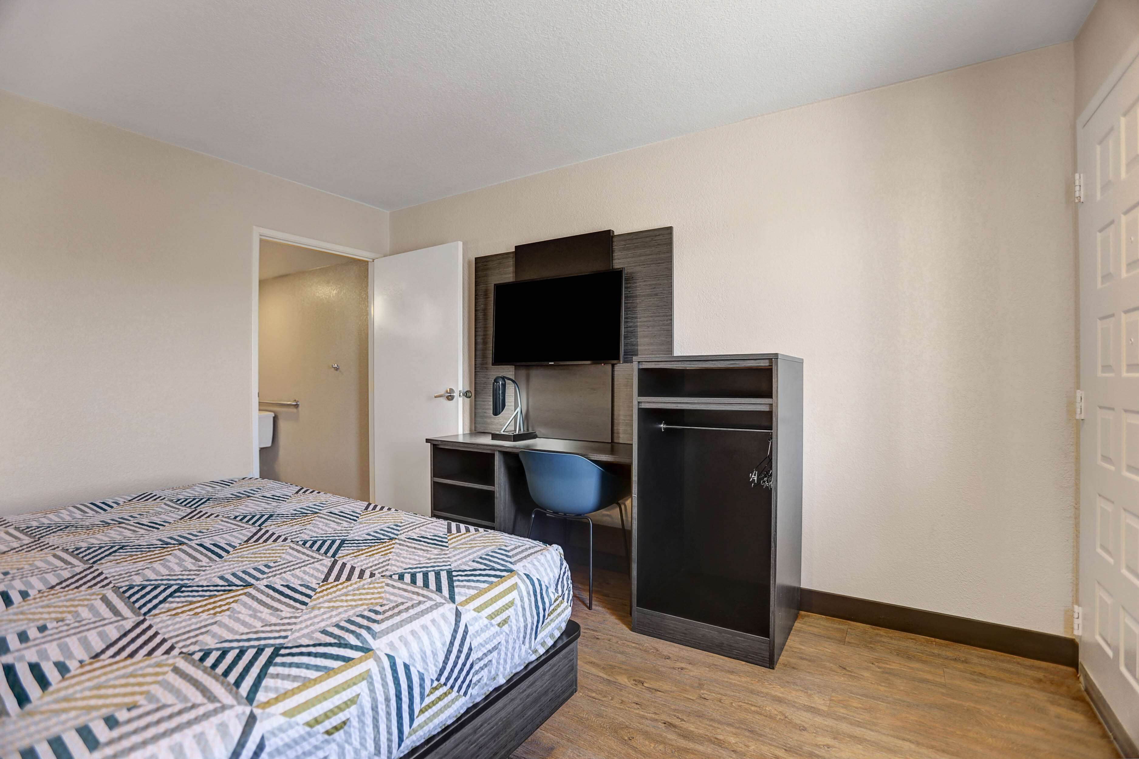 A hotel room with a bed, a desk, a chair, a TV, and a wardrobe.